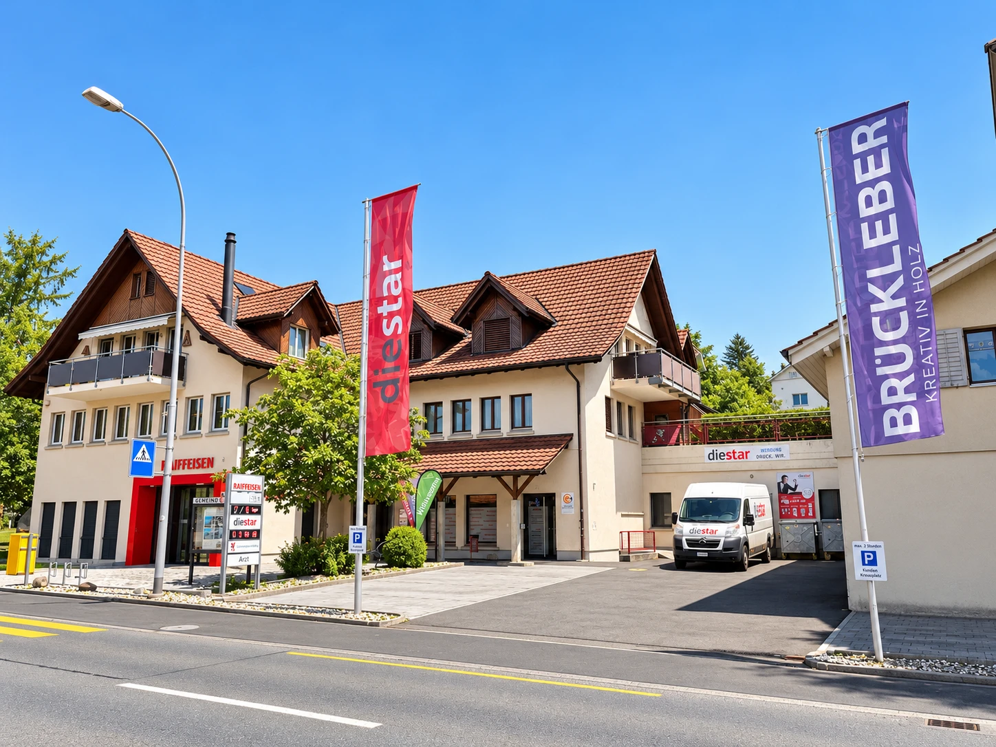 Gebäude am Kreuzplatz 1 in Aesch LU mit Fahnenmasten, Beachflags und Parkplätzen direkt an der Hauptstrasse