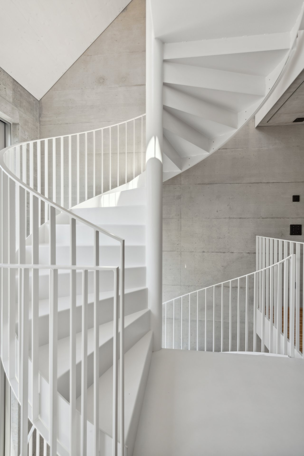 Weisse Wendeltreppe aus Stahl vor Sichtbetonwand