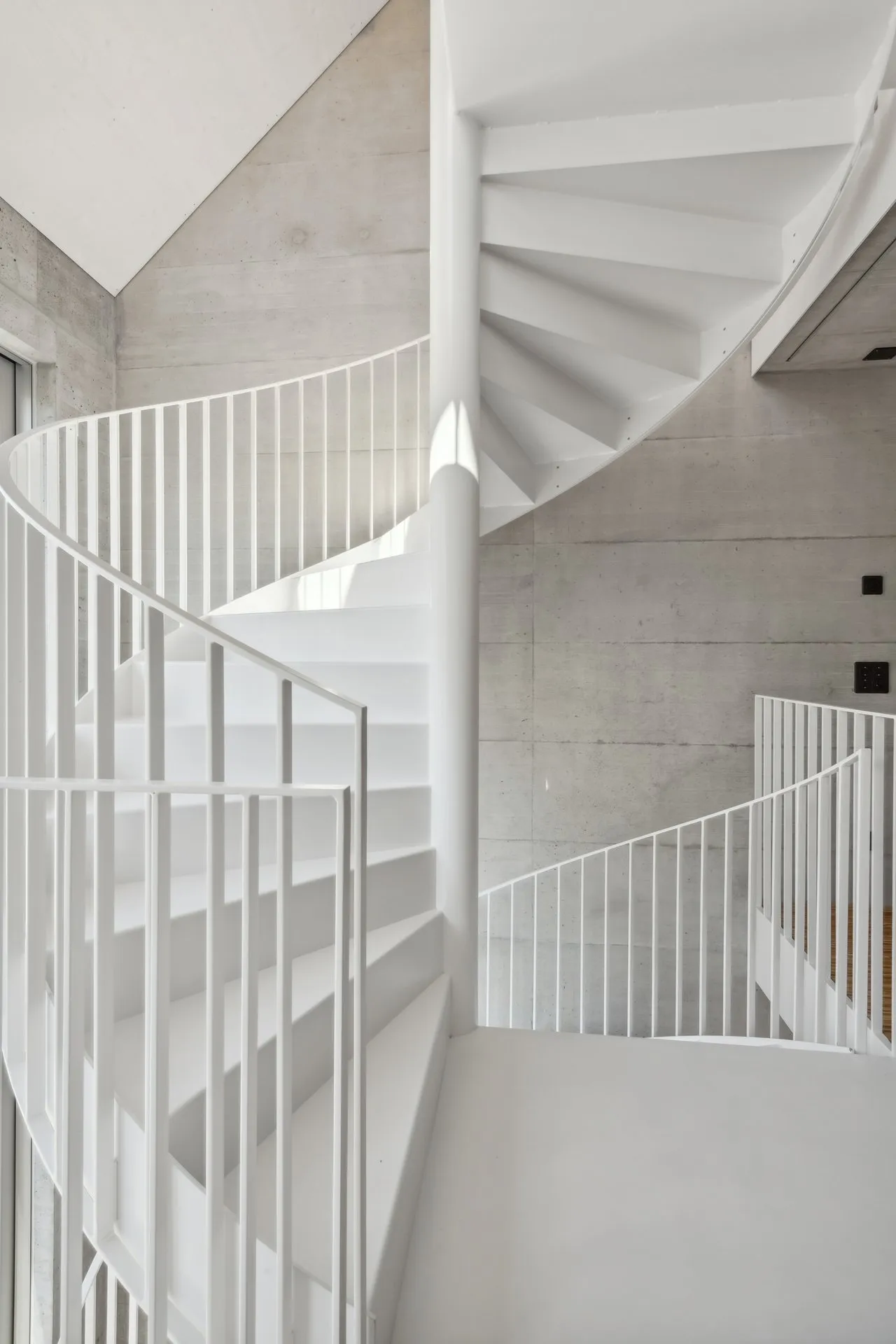 Weisse Wendeltreppe aus Stahl vor Sichtbetonwand