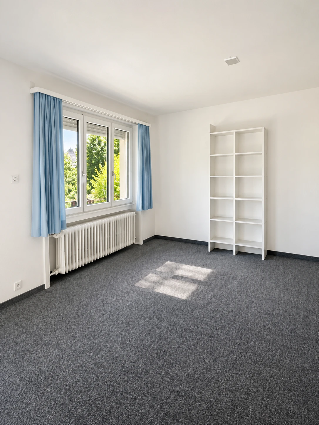 Zimmer im Obergeschoss mit Fenster zum Garten, Teppichboden und Radiator, bildlich aufbereitet